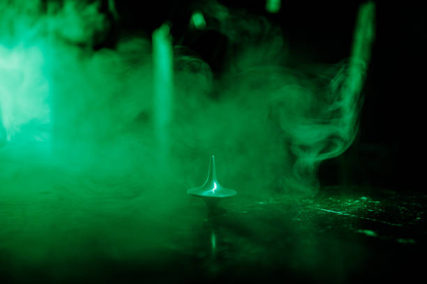 istock Totem spinning top spinning, wobbling and stopping. Spinning top on mirror surface with toned smoke background light. Whirligig in action in dark room on table. 963433128