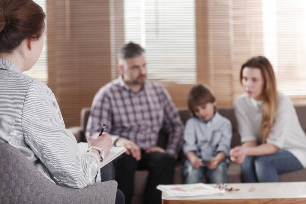 rückansicht des weiblichen psychologen helfen, junge familie mit einem kind, kind-entwicklung-probleme zu lösen. familie sitzt auf einem sofa in den unscharfen hintergrund - mental health professional family couple psychiatrist stock-fotos und bilder