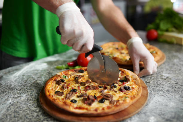 シェフは、木製基板に焼きたてのピザをカットします。 - cheese making ストックフォトと画像