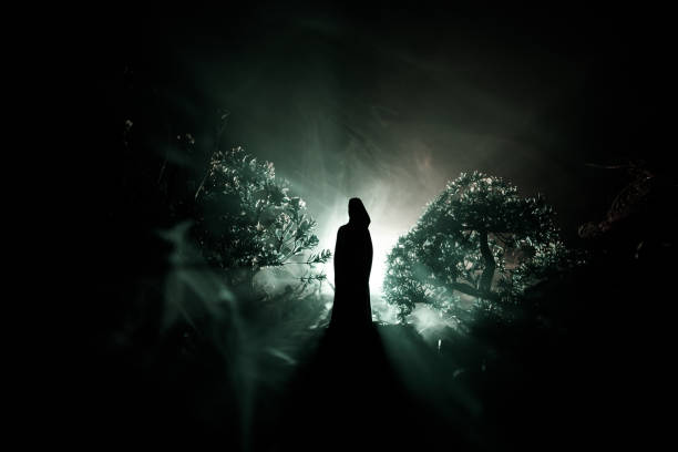 istock Horror Halloween decorated conceptual image. Alone girl with the light in the forest at night. Silhouette of girl standing between trees with surreal light . Selective focus. 963437696