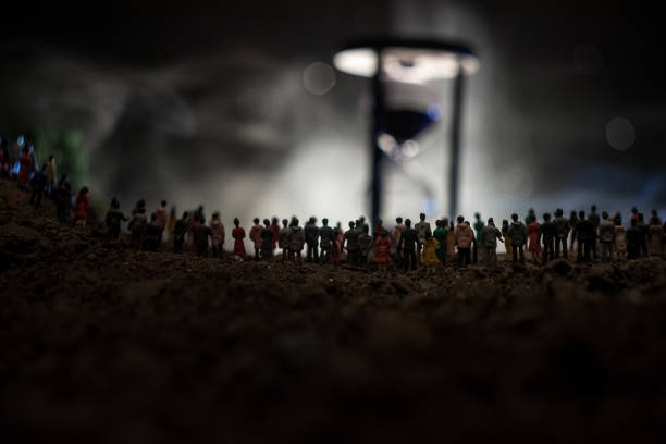 Silhouette of a large crowd of people in forest at night standing against a big hourglass with toned light beams on foggy background. Time concept. Silhouette of a large crowd of people in forest at night standing against a big hourglass with toned light beams on foggy background. Time concept. Hourglass measuring the passing time cologne germany stock pictures, royalty-free photos & images