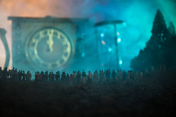Silhouette of a large crowd of people in forest at night standing against a big arrow clock with toned light beams on foggy background. Time concept. Silhouette of a large crowd of people in forest at night standing against a big arrow clock with toned light beams on foggy background. Time concept. Hourglass measuring the passing time cologne germany stock pictures, royalty-free photos & images