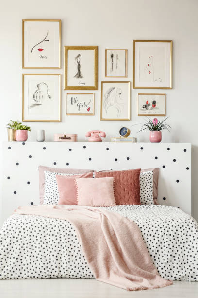 istock Front view of a king size bed with pink pillows, dotted sheets, headrest with decorations and paintings on the wall in a bedroom interior 963447280