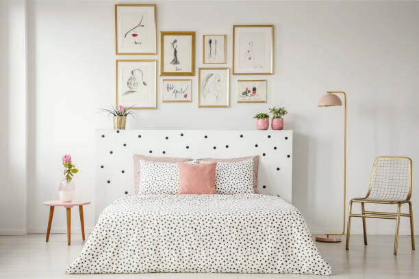 istock Bright bedroom interior with dotted sheets and headrest, double bed, gold accents and art gallery above 963447296