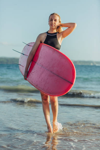 istock beautiful female surfer with surfboard on beach 963449878