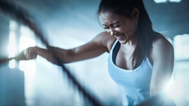 istock Athletic Female in a Gym Exercises with Battle Ropes During Her  Workout/ High-Intensity Interval Training. She's Muscular and Sweaty, Gym is in Industrial Building. 963452440
