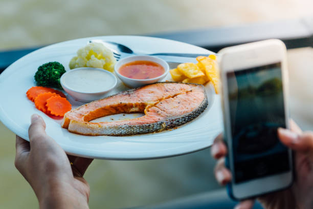 woman hand holding smartphone and take photo of salmon steak on white dish with seasoning sauce and vegetable in restaurant - food dinner prepared fish gourmet imagens e fotografias de stock