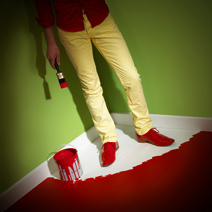 YOUNG MAN WEARING YELLOW JEANS TRAPPED IN CORNER OF ROOM BY WET RED PAINT ON FLOOR