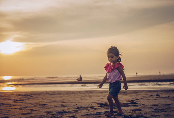 This image captures the joyful moment of a young girl running along the sandy beach, her vibrant red dress billowing in the breeze.