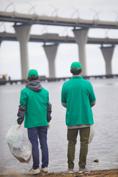 Green men Back view of two men in green uniform standing by river while picking up litter on its bank greenpeace activists stock pictures, royalty-free photos & images