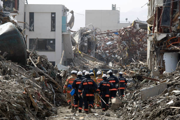 Never End Environmental Disaster Rescue Team searching operation on debris and mud covered at Tsunami hit Destroyed city in Rikuzentakata on March 20, 2011, Japan.  On 11 March 2011, an earthquake hit Japan with a magnitude of 9.0, the biggest in the nation's recorded history and one of the five most powerful recorded ever around the world. Within an hour of the earthquake, towns which lined the shore were flattened by a massive tsunami, caused by the energy released by the earthquake. With waves of up to four or five metres high, they crashed through civilians homes, towns and fields. honshu stock pictures, royalty-free photos & images