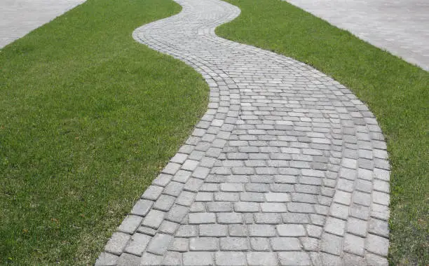 Photo of Curved path in the shape of a wave on the grass in the Park. Paved with tiles of different shapes.