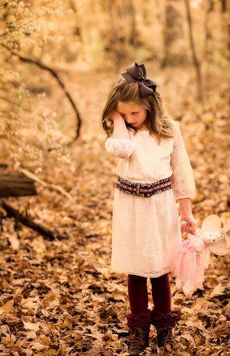 Young innocent girl with a bow in her long brown hair is scared and afraid lost in the woods on an Autumn day, Indiana, USA