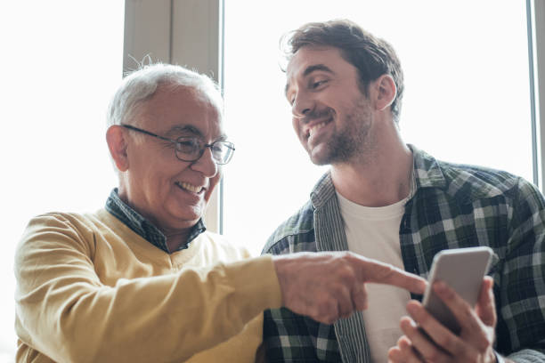 istock Happy young man holding phone and elderly man pointing at it 963543290