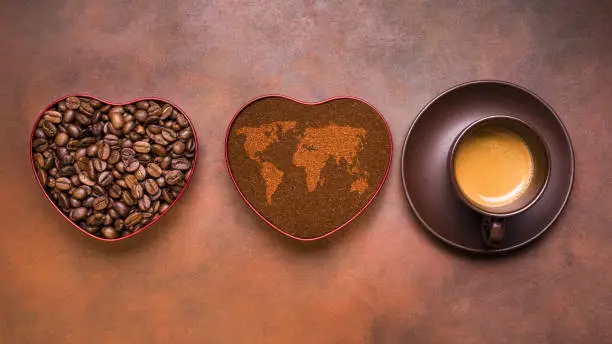 a cup of creamy espresso coffee, ground coffee and roasted beans in a heart-shaped bowl with a map of the world