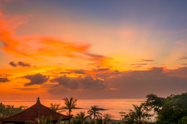 Indonesia. Bali island. Colorful sunset sky over the ocean and beach. Boats, palm trees and traditional roof