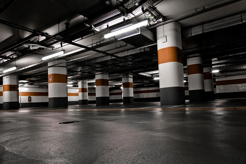 Empty underground garage interior with concrete walls and floor, white ceiling lights and small windows in the background. 3D rendered image.