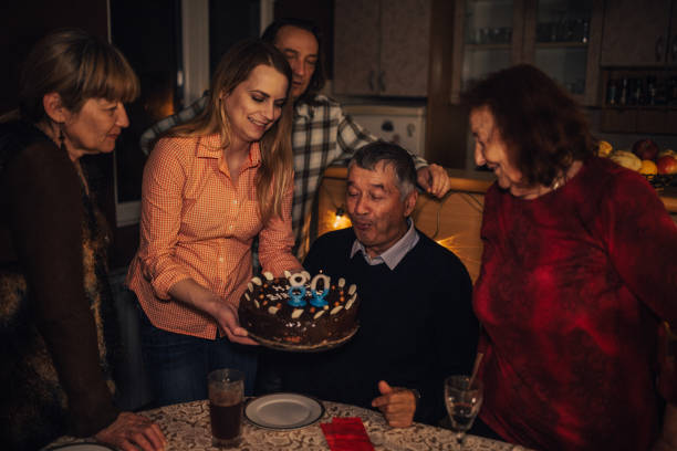 großvater bläst kerzen und feiert seinen geburtstag mit familie - long life cake birthday cake grandparent stock-fotos und bilder