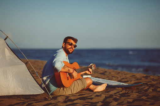 Man sitting on the beach singing and playing guitar