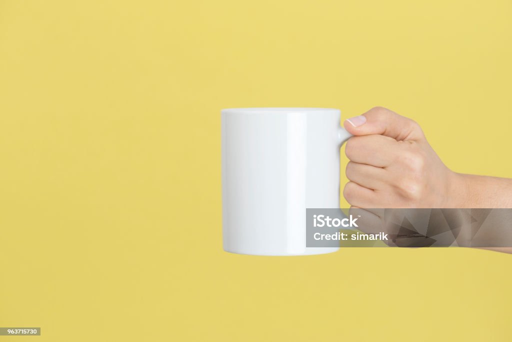 Relaxing Caucasian female is holding a white coffee mug in hand in front of a yellow background. Mug Stock Photo