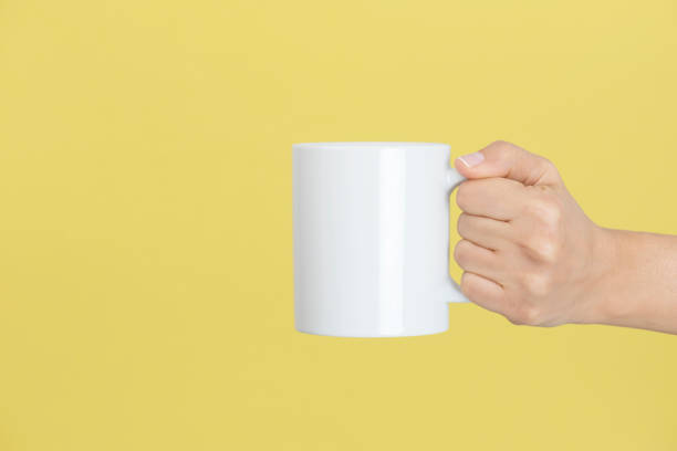 Relaxing Caucasian female is holding a white coffee mug in hand in front of a yellow background. mug stock pictures, royalty-free photos & images