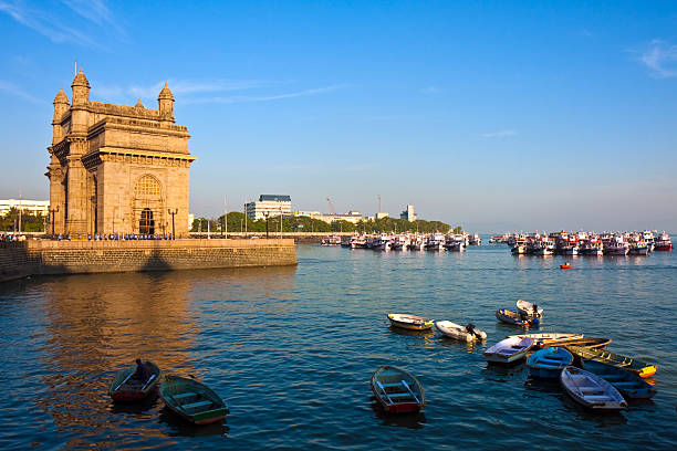 Gateway of India monument in Mumbai at sunset Gateway of India in Mumbai during sunset.  There are several small boats in blue water and a castle-like building towards the left.  There is land visible in the distance. maharashtra stock pictures, royalty-free photos & images