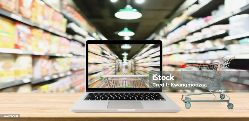 Supermarkt-Gang unscharf Hintergrund mit Laptop-Computer und Wagen auf Holztisch Online-shopping-Konzept - Lizenzfrei Internet Stock-Foto