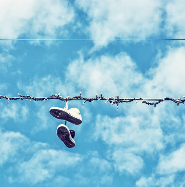 Pair of old shoes hang on power line against blue sky, space for text.