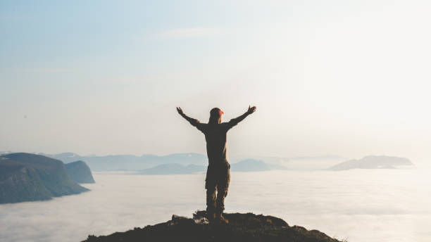 Young man stand on top of mountain top with hands raised in the air. Success and risk concept. stock photo