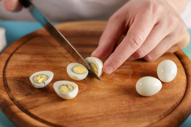 Man cuts boiled quail eggs on wooden cutting board close-up. stock photo