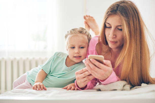 istock Mother and daughter using phone in bed 963811624