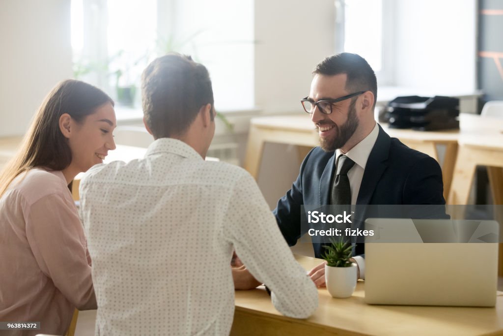 Friendly lawyer or financial advisor in suit consulting young couple Friendly lawyer or financial advisor in suit consulting young couple, smiling investment broker or bank worker making loan offer, giving legal advice, selling insurance or real estate to customers Bank - Financial Building Stock Photo