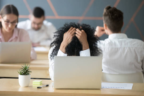 frustrated african-american woman feeling despair in shared office with laptop - unemployment fear depression women imagens e fotografias de stock