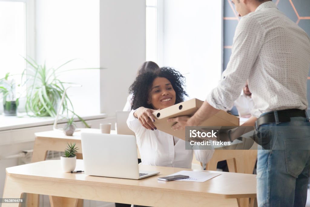Smiling african employee taking pizza from courier, office food delivery Smiling young african american woman employee taking pizza box from courier sitting at work desk, black office worker ordered meal food delivery service on corporate lunch break sitting at workplace Box - Container Stock Photo