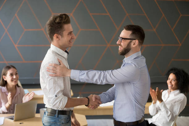Team leader handshaking employee congratulating with professional achievement or promotion Team leader handshaking employee congratulating with professional achievement or career promotion, thanking for good project result while team supporting applauding, appreciation recognition concept in pride we trust stock pictures, royalty-free photos & images