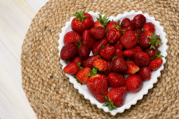 istock LOOKING DOWN FROM ABOVE FRESHLY CLOSE UP RIPE STRAWBERRIES SERVED ON A HEART WHITE PLATE WITH A JUTE CLOTHTABLE 963815144