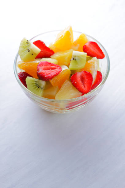 istock Fruit salad from pineapple, kiwi, orange, strawberry. Multicolored sliced fruit in a transparent dish. Vegetarian meal on a white background. Copy space. 963827548