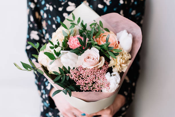 mujer muy bonita floristería hermoso colorido flor flor bouquet de rosas frescas de arenas movedizas, claveles, ranunculus, peonía, hojas de pistacho sobre el fondo gris de la pared - florist women bouquet spring fotografías e imágenes de stock