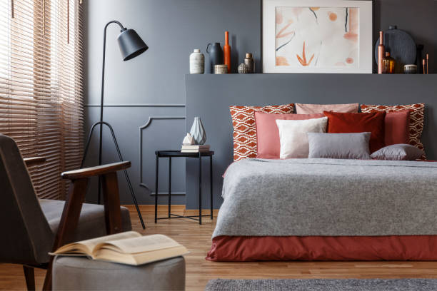 gros plan un livre sur un tabouret à côté d’un fauteuil dans un intérieur de chambre à coucher avec un lit douillet avec oreillers, de peinture et de lampe - spice store photos et images de collection