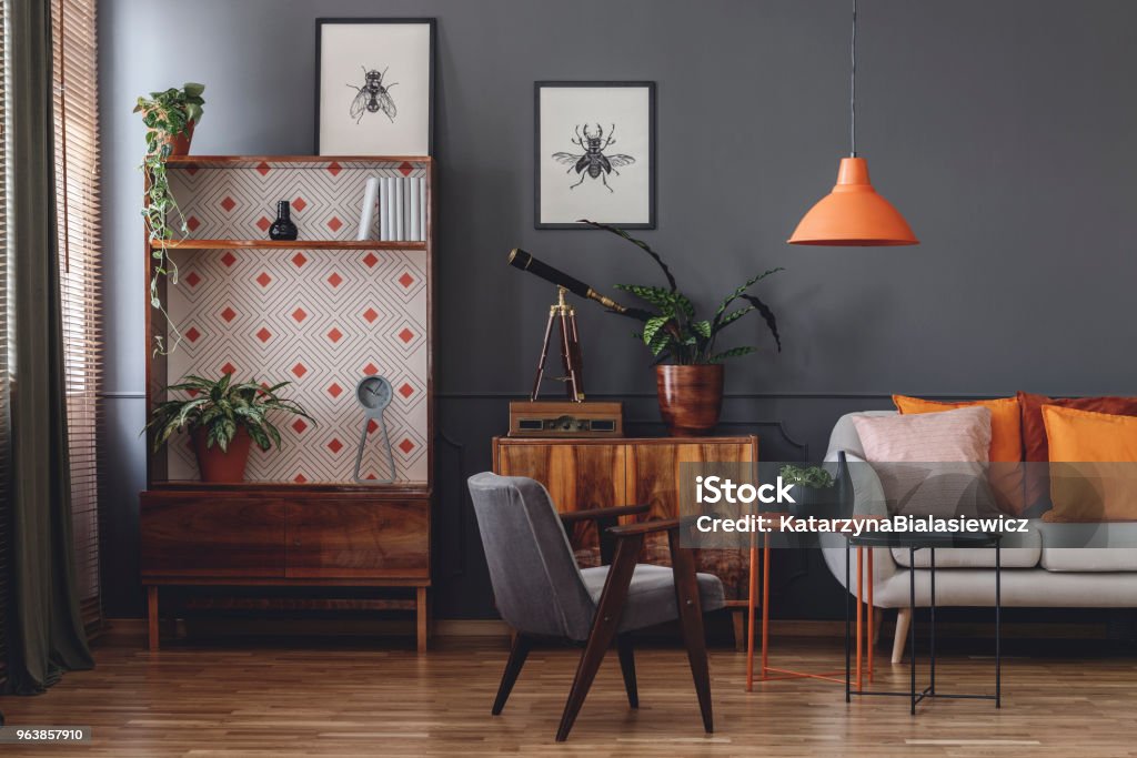 Vintage grey living room interior Posters on grey wall in vintage living room interior with wooden armchair next to orange table with plant Living Room Stock Photo