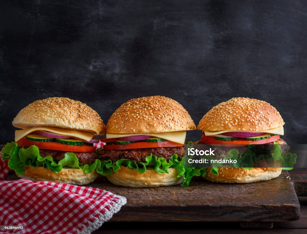 Hamburger with beef, cheese and vegetables Hamburger with beef, cheese and vegetables on rustic wooden  brown cutting board, closeup American Culture Stock Photo