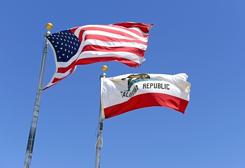 California state flag and American flag with blue sky background, waving in the wind