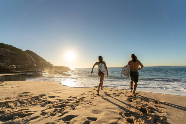 Happy couple having fun surfing at the beach Happy couple having fun surfing at the beach and running towards the sea holding their board - summer lifestyle concepts sports training australia stock pictures, royalty-free photos & images