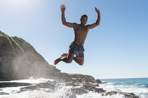 Happy man having fun jumping at the beach and enjoying the summer  - fitness cocnepts