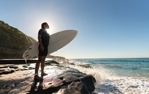 Beautiful female surfer at the beach holding a surfboard and wearing a wetsuit â summer lifestyle concepts