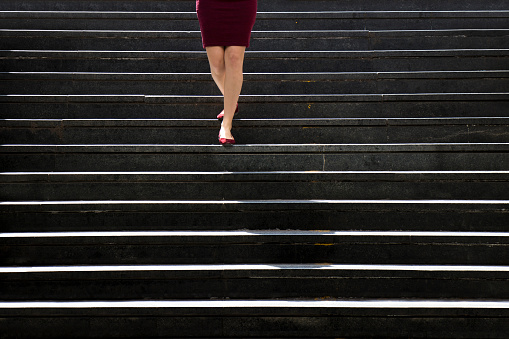 Legs of a young woman in red shoes and dress approaching while walking down the city public stairs