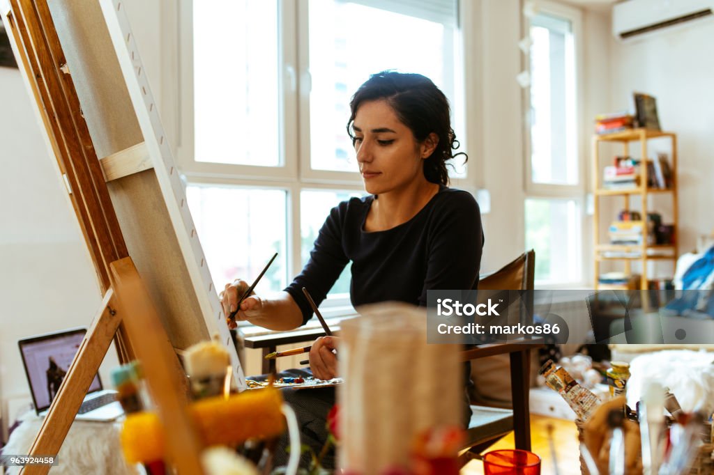 Beautiful female artist painting on a canvas with brush and palette Beautiful female artist painting on a canvas with brush and palette in her studio 20-29 Years Stock Photo