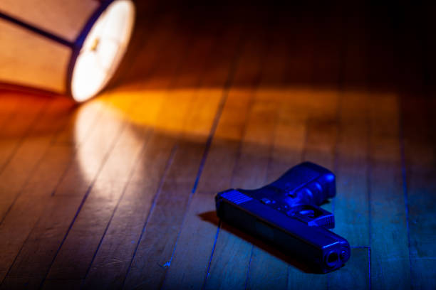 A firearm lays on the wood floor in front of a lamp which has been knocked over.