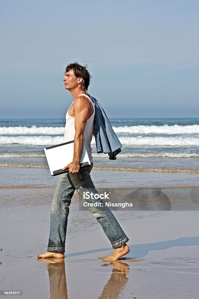 Cara jovem caminhando com seu laptop na praia - Foto de stock de A caminho royalty-free