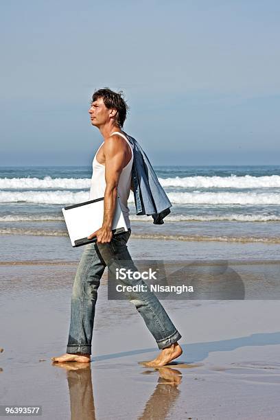 Foto de Cara Jovem Caminhando Com Seu Laptop Na Praia e mais fotos de stock de A caminho - A caminho, Adulto, Adulto maduro